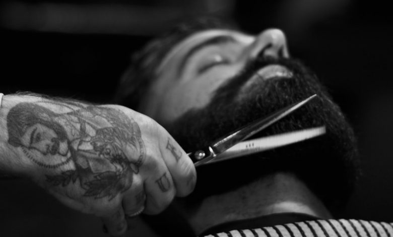 grayscale photography of person holding scissor clipping man's beard